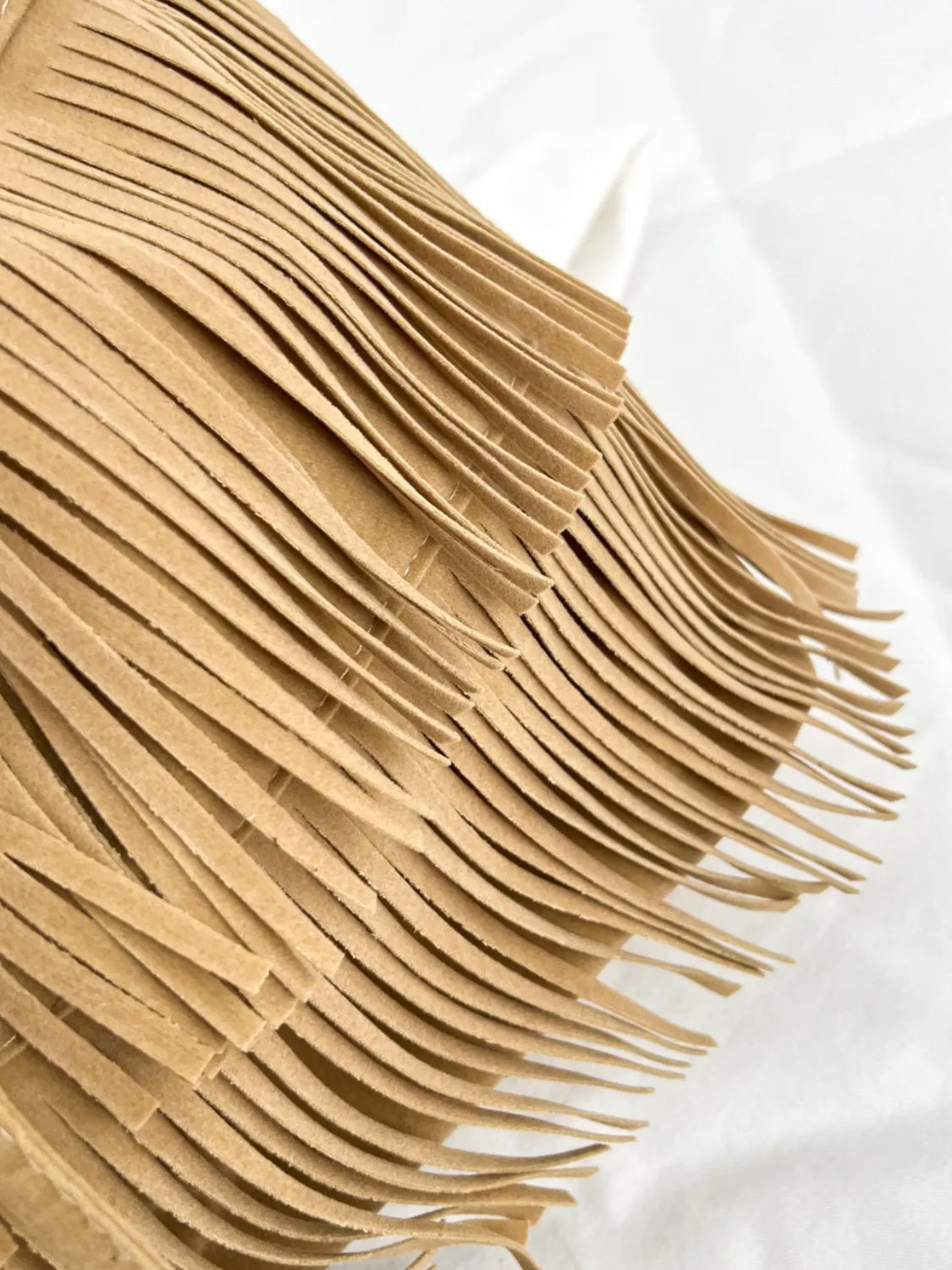 Detalle de un bolso de hombro elegante con flecos en color beige para un look moderno